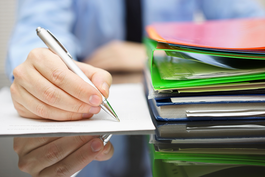 Audit Documents A businessperson takes notes and reviews a stack of documents in a folder.