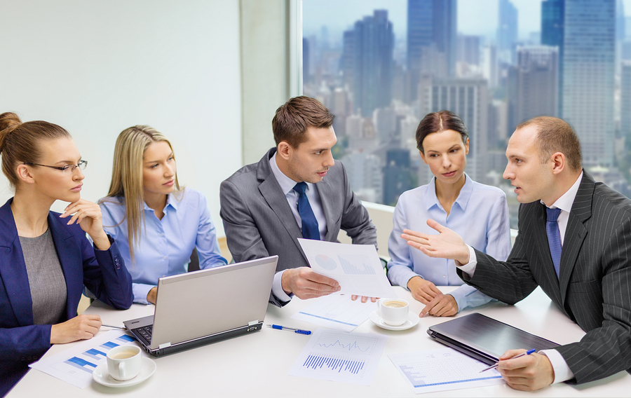 An executive team reviews documents, laptops and mobile devices.