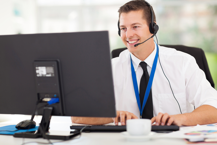 A technical support worker speaks through a headset phone while working on a computer.