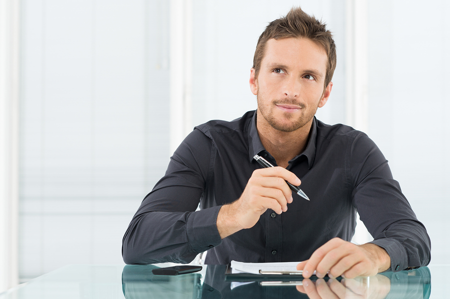 A businessman is pondering and writing down his thoughts on a notepad.