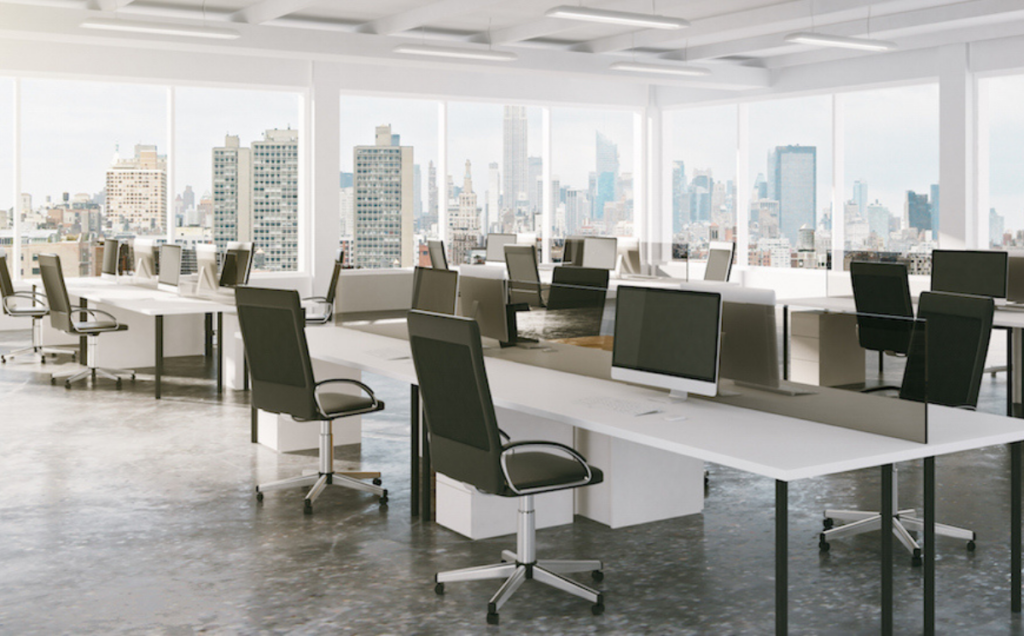 A modern open‑plan office with rows of white desks, large computer monitors, and black office chairs. Floor‑to‑ceiling windows surround the space, showing a bright city skyline in the background.