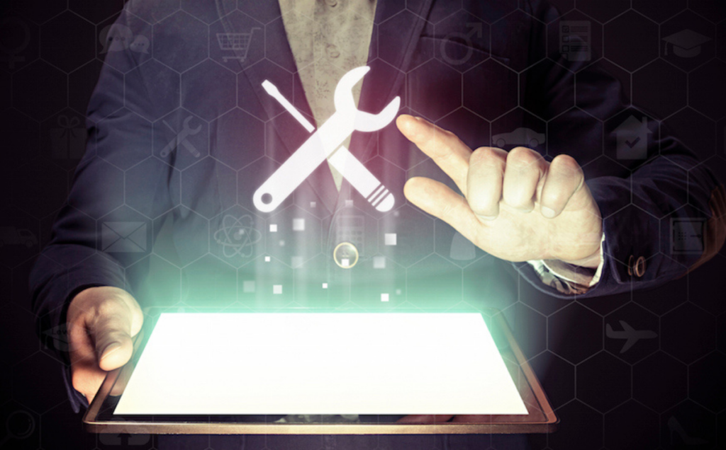 A person in a suit holds a tablet with a glowing screen while a holographic wrench and screwdriver icon floats above it, surrounded by faint hexagonal digital symbols representing various services and technology.