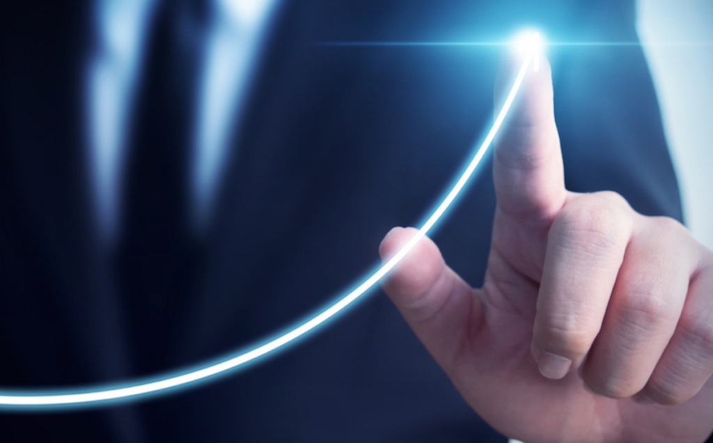A person in a dark suit touches a glowing upward‑curving line, symbolizing growth or rising performance.