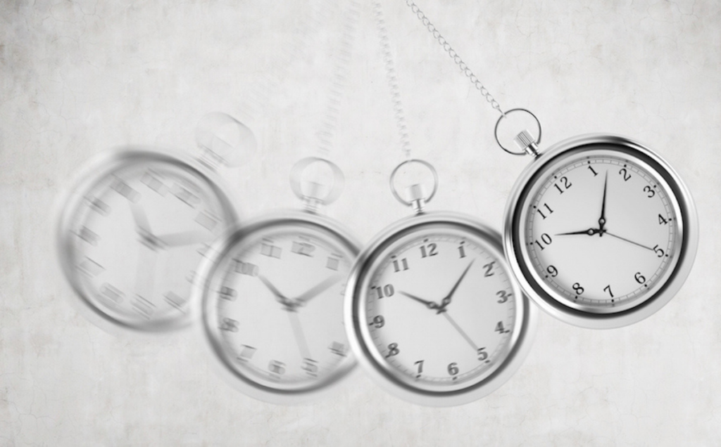 A silver pocket watch swings in multiple blurred positions, showing motion against a light textured background, with its chain visible at the top.
