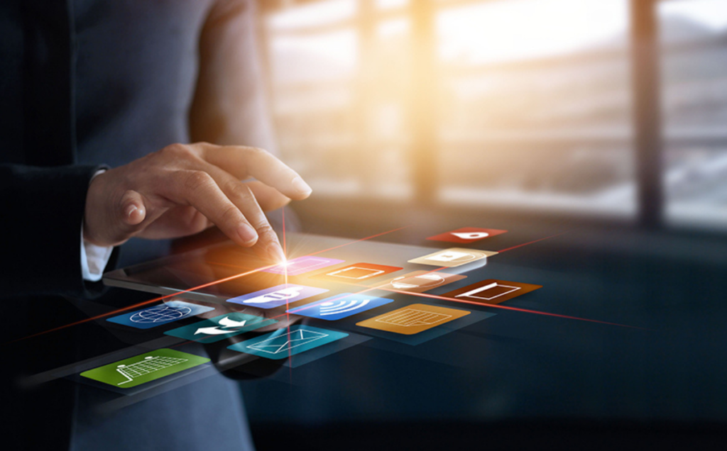 A person in formal attire uses a tablet that projects colorful holographic app icons, including symbols for communication, data sharing, and Wi‑Fi, set against a softly lit modern office background.